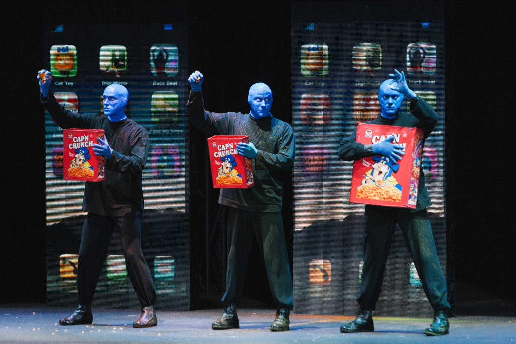 Two Blue Men hold up handfuls of cereal, while the third holds up a single piece. | Cam Peters