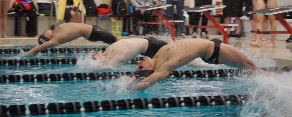 Sporting black caps, SU swimmers Jason Klein (Right) and Morgan Montemayor (Left) launch off the swim blocks to start a backstroke race.