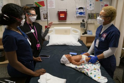 Nursing students Rosalie Monkono (left) and Kennedy Johnson (right) receive instruction on swaddling a newborn from professor Jenny Curwen (middle).