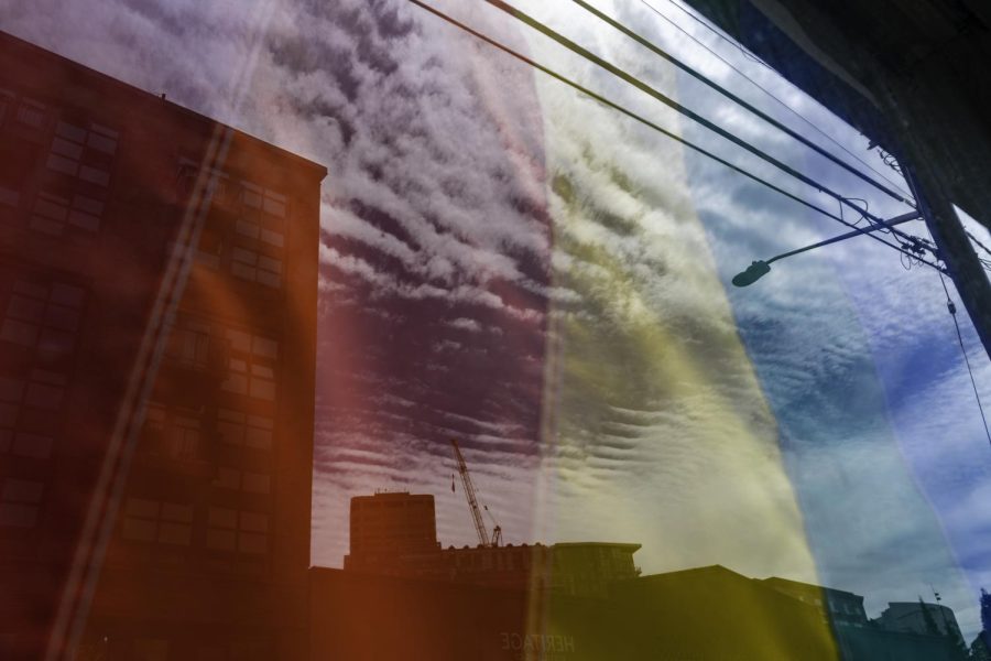 The Seattle skyline reflected in a window with a Pride flag hanging. 