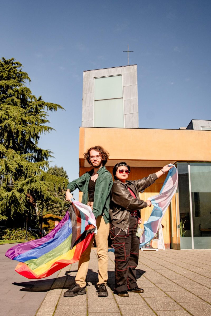 Pride in motion: third-year Seattle University Students, Rose (they/them) and Gabi (they/them), wave their flags in front of St. Ignatius Chapel.