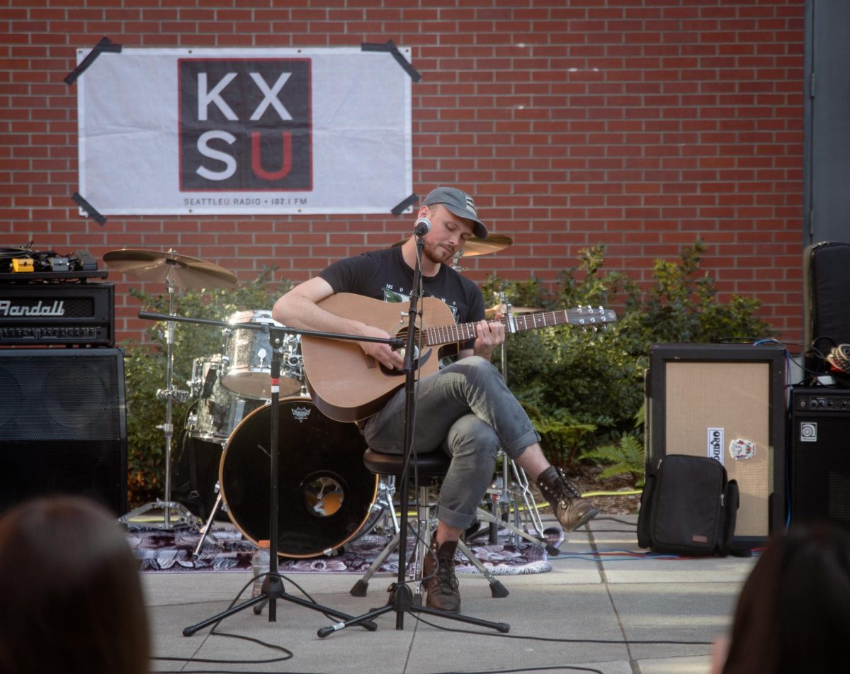 Jacob Kelly (he/him), lead singer and guitarist from Lowe Cellar, performing at the Sinegal Patio.