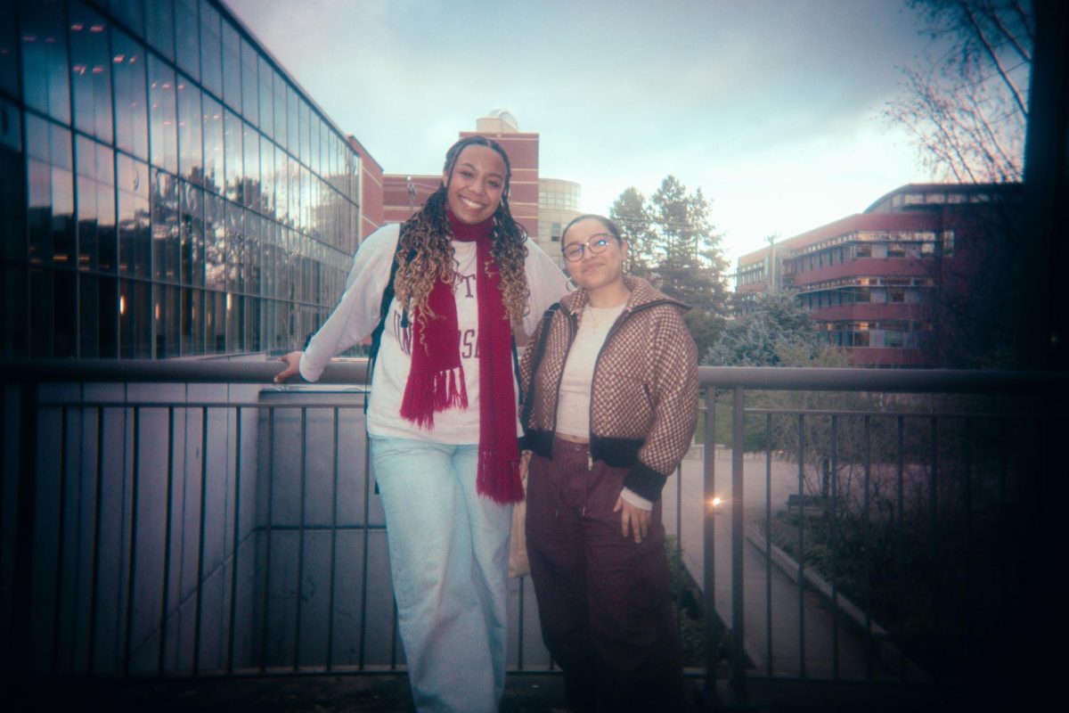 Two students - one in a cropped brown jacket and the other in a striking red scarf - stand outside the Student Center