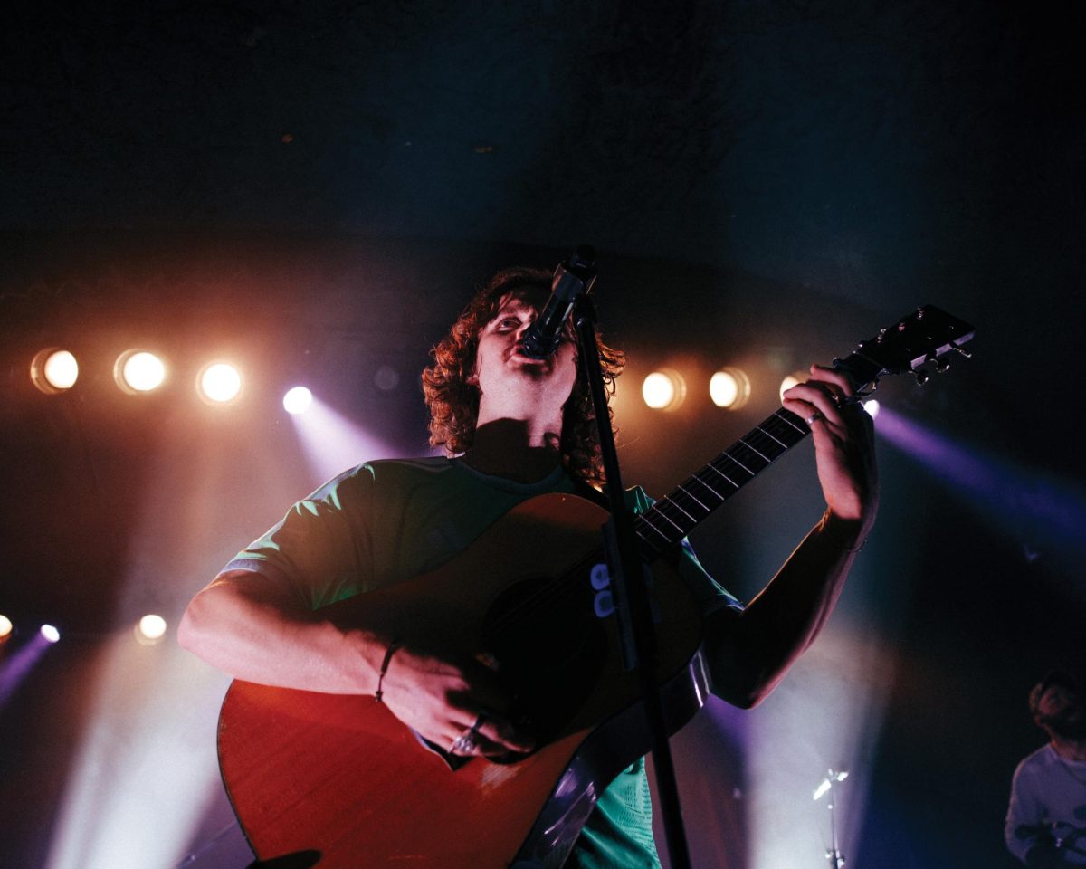 Evan Honer sings into the microphone while playing his guitar.