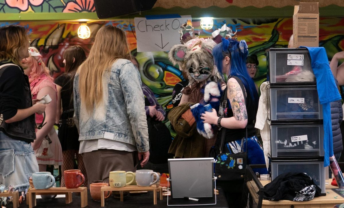 A person in a fursuit head glances at hand-made mugs.